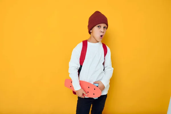 Cool leende pojke med röd ryggsäck röd skateboard gul färg bakgrund — Stockfoto