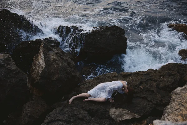 Женщина лежит на скалистом побережье с трещинами на скалистой поверхности ландшафта — стоковое фото