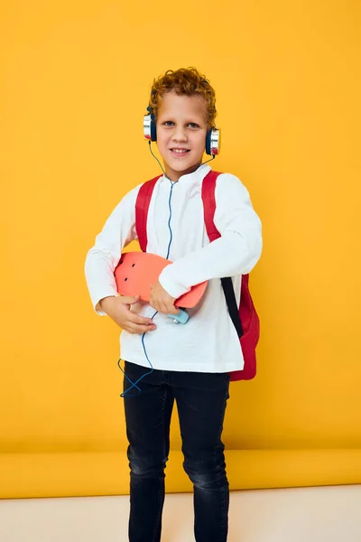 Snygg pojke med skateboard i hörlurar gul bakgrund — Stockfoto
