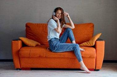 Güzel bir kadın evdeki kanepede oturmuş kulaklıkla müzik dinliyor.