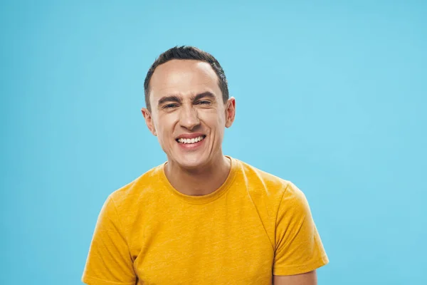 Man in een geel t-shirt op een blauwe achtergrond emoties grimas — Stockfoto