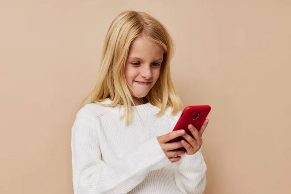 Pequeña chica linda comunicación teléfono inteligente entretenimiento en un fondo beige —  Fotos de Stock