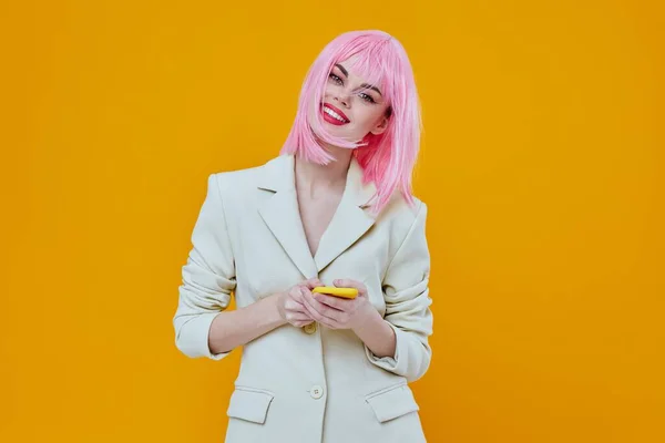 Wesoła kobieta z różowymi włosami z telefonem w białym garniturze żółte tło — Zdjęcie stockowe
