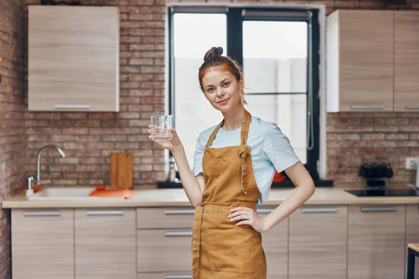 Hermosa mujer en un delantal vaso de agua en la cocina quehaceres domésticos vida en casa — Foto de Stock