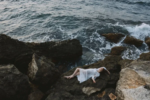 Beautiful woman in a white dress lying on a stone in a white dress view from above — Stock Photo, Image