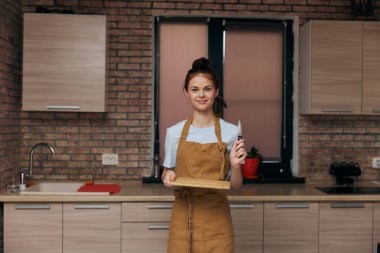 Mutfakta önlüklü güzel bir kadın. Bıçaklı tahta kesiyor. Modern tarzda.