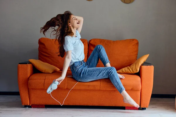 Mulher alegre sentado no sofá em casa ouvir música em fones de ouvido inalterado — Fotografia de Stock