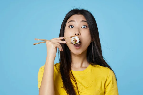Asiatin im gelben T-Shirt Essstäbchen Sushi-Rollen — Stockfoto