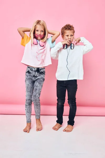 Retrato de uma menina e um menino crescimento completo usando fones de ouvido fundo rosa — Fotografia de Stock