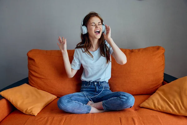 オレンジ色のソファの上でヘッドフォンで音楽を聴く陽気な女性ライフスタイル — ストック写真