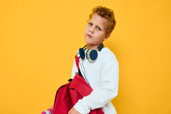 Stylowy chłopiec z czerwonym plecakiem noszącym słuchawki żółte tło — Zdjęcie stockowe