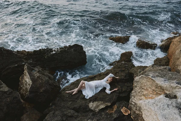 Hermosa novia acostada en la costa rocosa con grietas en la superficie rocosa inalterada — Foto de Stock