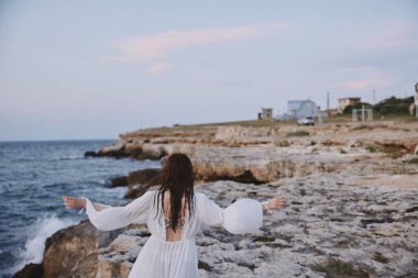 Kumsalda yürüyen, beyaz elbiseli, ıslak saçlı bir kadın.