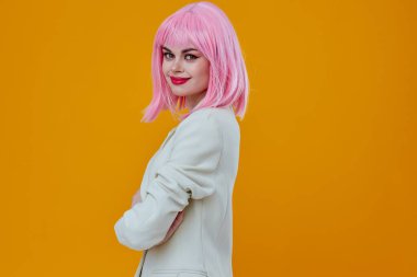 Beyaz elbiseli kadın, sarı arka planda pembe peruk takıyor.