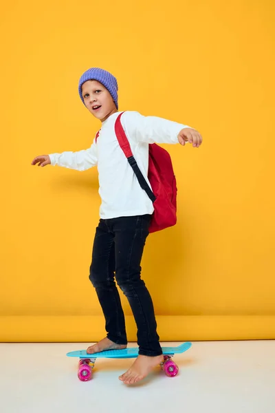 可愛い男の子の肖像画青い帽子の黄色の背景にスケートボードに乗る — ストック写真