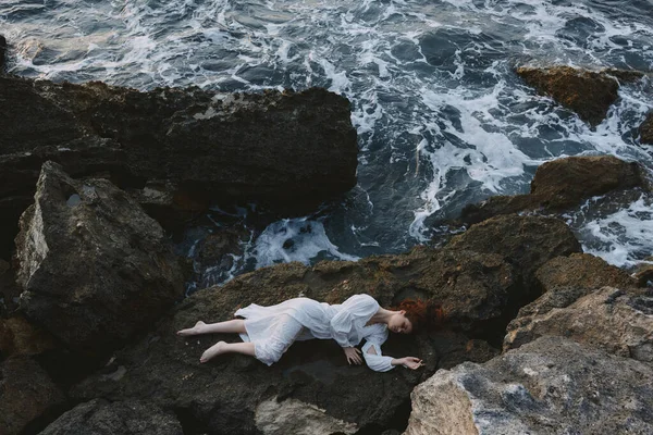 Barefoot woman in a secluded spot on a wild rocky coast in a white dress unaltered — 图库照片