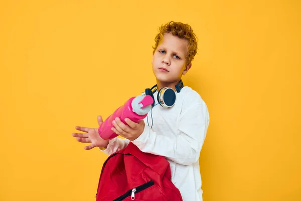 Iskola fiú rózsaszín víz palack öröm szórakozás fejhallgató pózol elszigetelt háttér — Stock Fotó