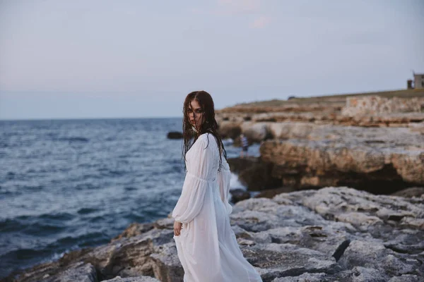 Femme aux cheveux mouillés dans une robe sur le rivage pierreux de l'océan — Photo