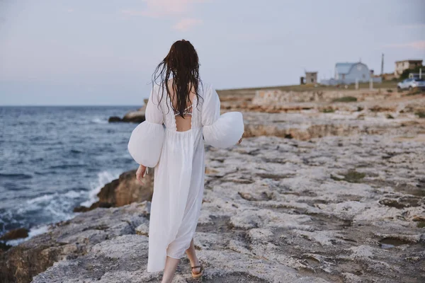 Γυναίκα περπάτημα σε λευκό φόρεμα στην παραλία πέτρα — Φωτογραφία Αρχείου