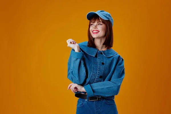 Mujer bonita en una gorra y chaqueta de mezclilla posando fondo amarillo inalterado —  Fotos de Stock