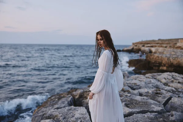 Beyaz elbiseli bir kadın okyanus taşından kumsalda geziniyor. — Stok fotoğraf