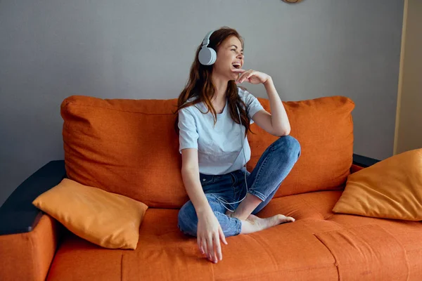 オレンジ色のソファの上でヘッドフォンで音楽を聴く女性 — ストック写真