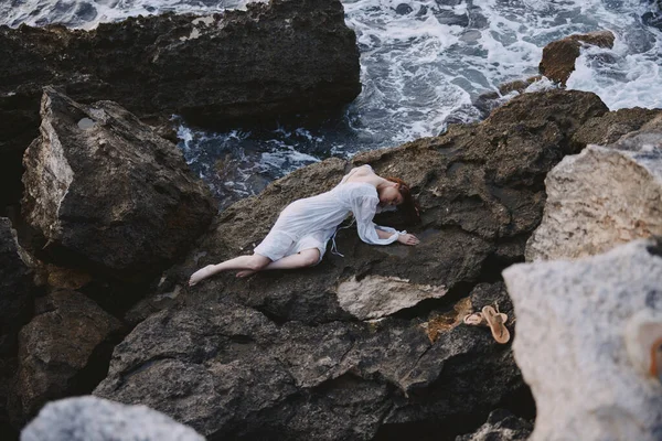 長い白いドレスを着た女が岩だらけの崖の上に寝そべって — ストック写真