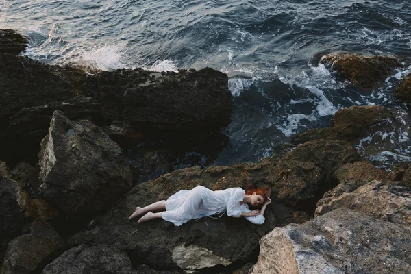 Босоногая женщина лежит на скалистом побережье с трещинами на скалистой поверхности природного ландшафта — стоковое фото