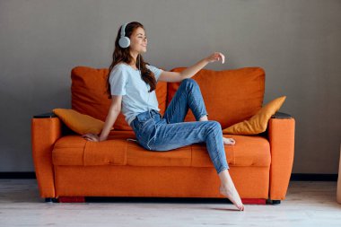 Neşeli kadın evdeki kanepede oturmuş hiç değiştirilmemiş kulaklıkla müzik dinliyor.