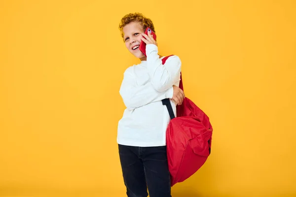 Glad skolpojke i vit tröja mobiltelefon röd ryggsäck isolerad bakgrund — Stockfoto