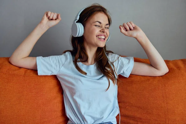 Bela mulher ouvindo música com fones de ouvido no sofá laranja apartamentos — Fotografia de Stock