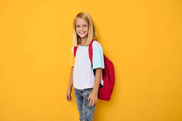 Chica de la escuela sonriente con una mochila roja de color amarillo de fondo — Foto de Stock