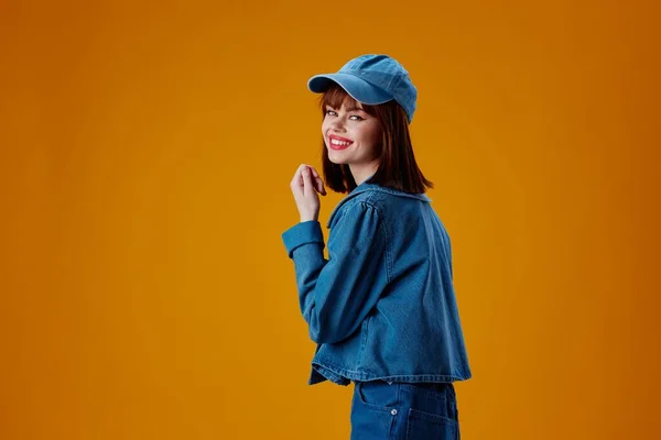 Pretty young female in a cap and denim jacket posing yellow background unaltered — Stockfoto