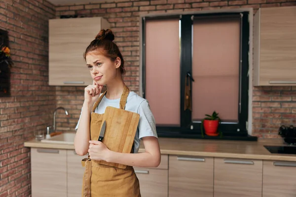 Bonita mujer en un delantal marrón tabla de cortar interior de la cocina inalterada — Foto de Stock