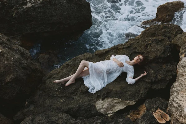 Beautiful bride in a secluded spot on a wild rocky coast in a white dress unaltered — Stock Photo, Image