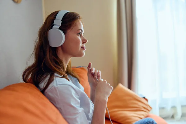 オレンジ色のソファ技術でヘッドフォンで音楽を聴く陽気な女性 — ストック写真