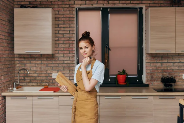 Mujer alegre en un delantal marrón tabla de cortar interior de la cocina inalterada — Foto de Stock