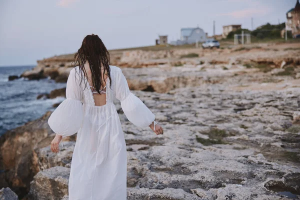 Islak saçlı, beyaz elbiseli, taşlı sahilli kadın. — Stok fotoğraf