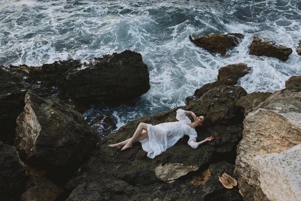 Barefoot woman Lies on his back on a stone cliff, cloudy weather view from above — 图库照片