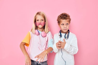 Pembe arka plan pozu veren kulaklık takan küçük bir çocuk ve kız.