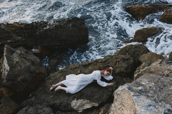 Uzun beyaz elbiseli, çıplak ayaklı, ıslak saçlı bir kadın kayalık bir uçurum kenarında yatıyor. — Stok fotoğraf