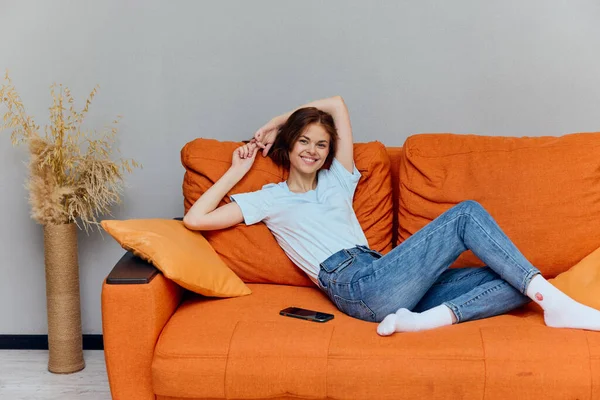 在橙色沙发上聊天的女人，带着智能手机，毫发无损 — 图库照片