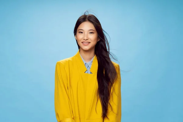 Mulher asiática aparência amarelo casaco sorriso azul fundo estúdio — Fotografia de Stock