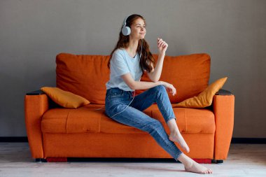 Turuncu koltukta kulaklıkla müzik dinleyen neşeli bir kadın.