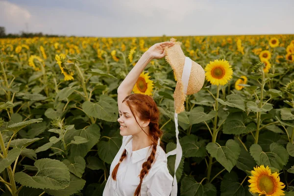 Frau mit zwei Zöpfen im Strohhut und weißem Kleid auf einem Feld mit Sonnenblumen — Stockfoto