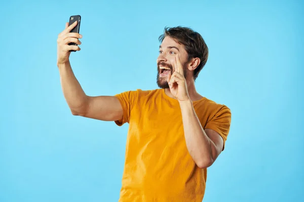 Man in geel t-shirt met een telefoon in zijn handen blauwe technologie achtergrond — Stockfoto