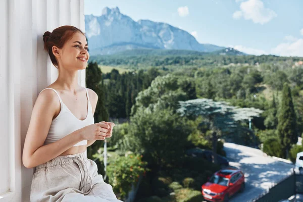 아름다운 여성 이 호텔 라이프 스타일의 열린 발코니에 있는 산들의 경치에 감탄하고 있습니다. — 스톡 사진