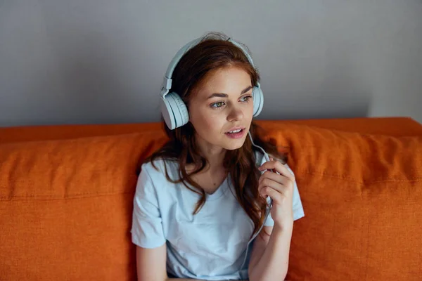ヘッドフォン技術で音楽を聴くオレンジのソファの女性 — ストック写真