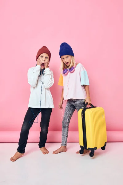 Sevimli küçük çocuklar şık kıyafetler bavul kulaklıklar pembe arka plan — Stok fotoğraf