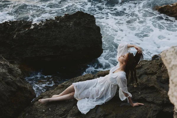 A woman in a white dress barefoot lies on a stone hold by her hair — Stock Photo, Image